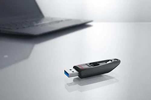 SanDisk Ultra USB 3.0 Flash Drive on a reflective surface next to a laptop.