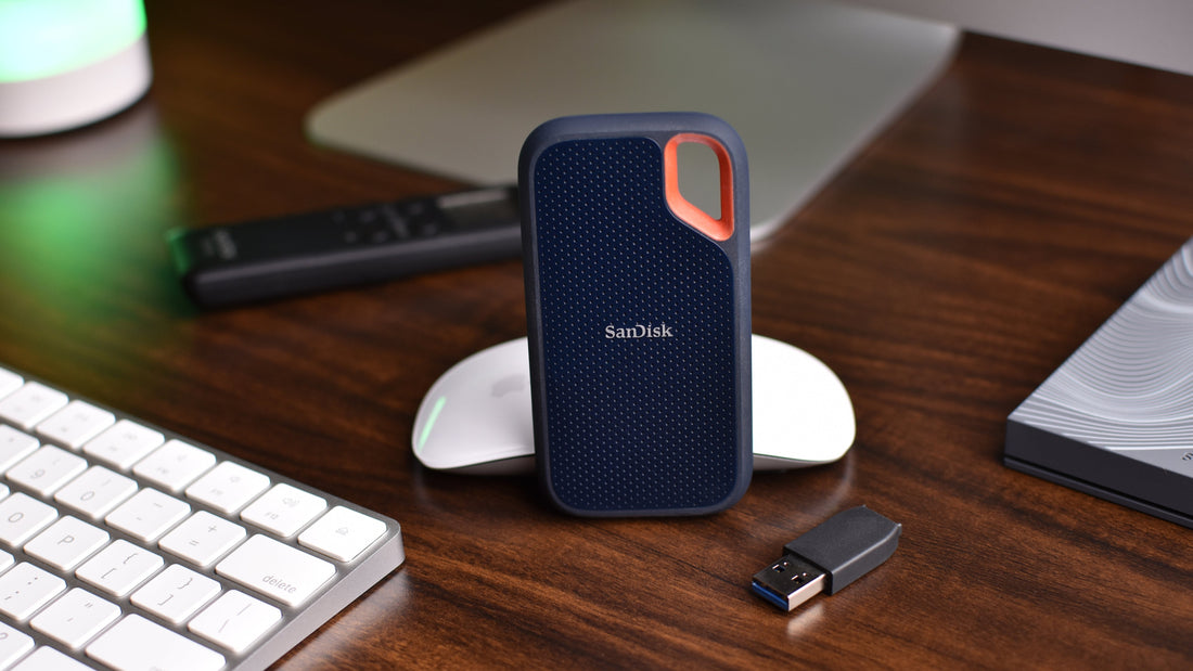 SanDisk portable external SSD on a desk beside a keyboard and USB drive — fast solid‑state storage for laptops and creators.